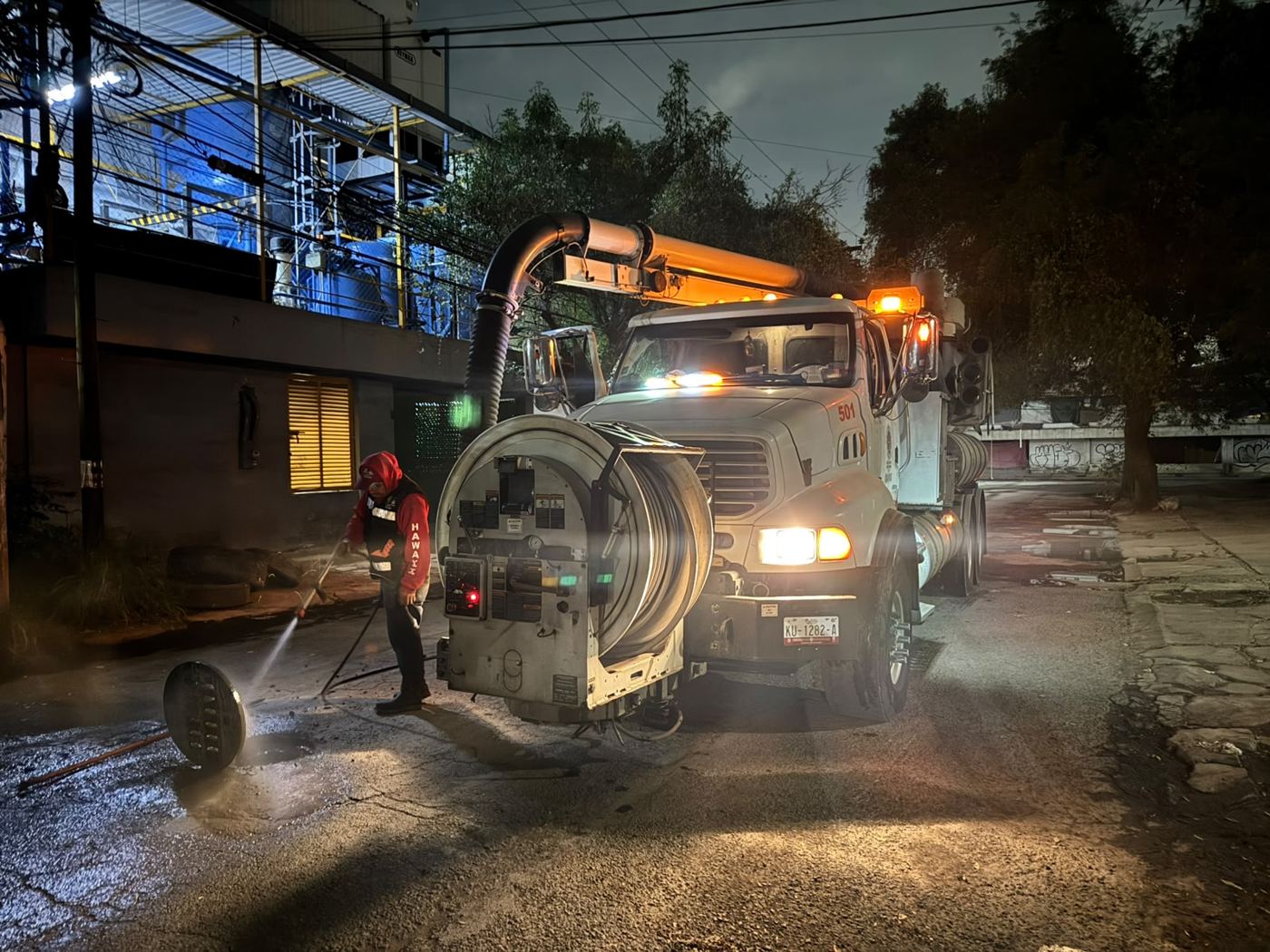 Operador lavando con chorro a presión un pozo de visita por la noche
